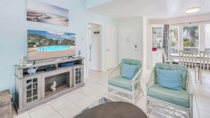 A living room with a TV, two chairs, a coffee table, and a poolside view.