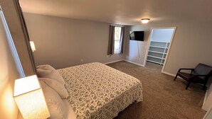 A bedroom with a bed, a chair, a TV, and a sliding door to a balcony.