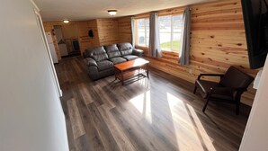 A cozy cabin interior with a wooden floor, a gray sofa, a wooden coffee table, and a TV mounted on the wall.