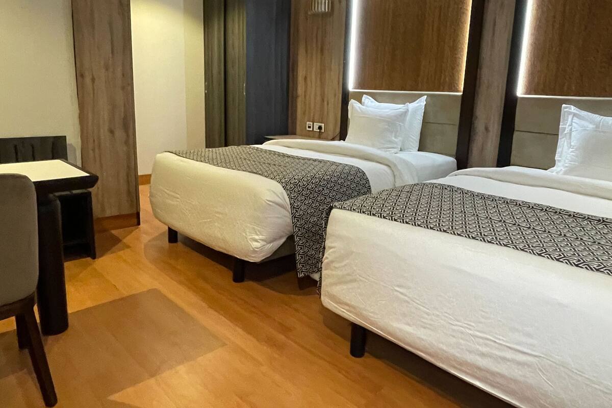 Quarto de hotel com duas camas, uma escrivaninha e uma cadeira.