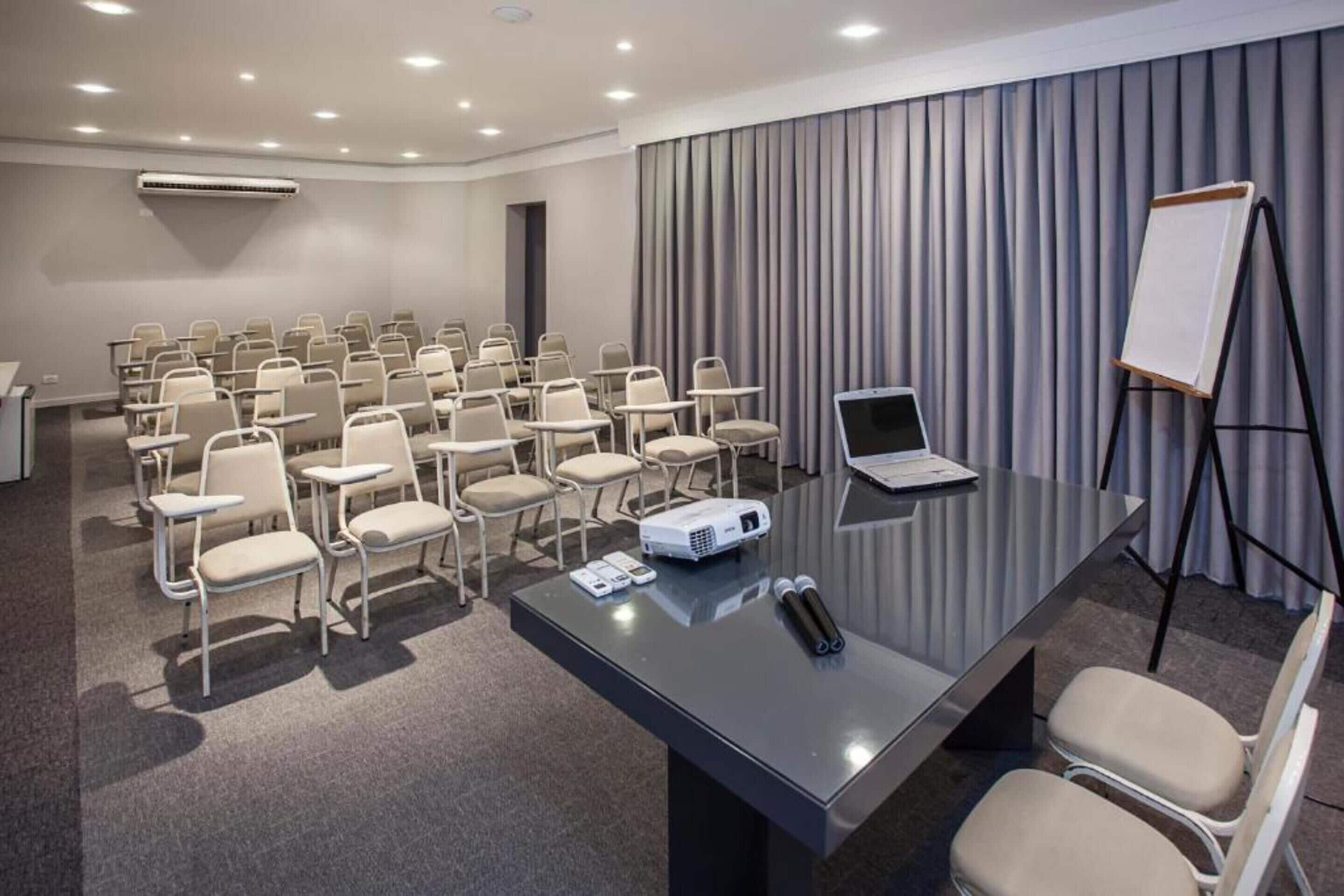 Une salle de conférence avec des rangées de chaises, un projecteur, un ordinateur portable et un tableau blanc.