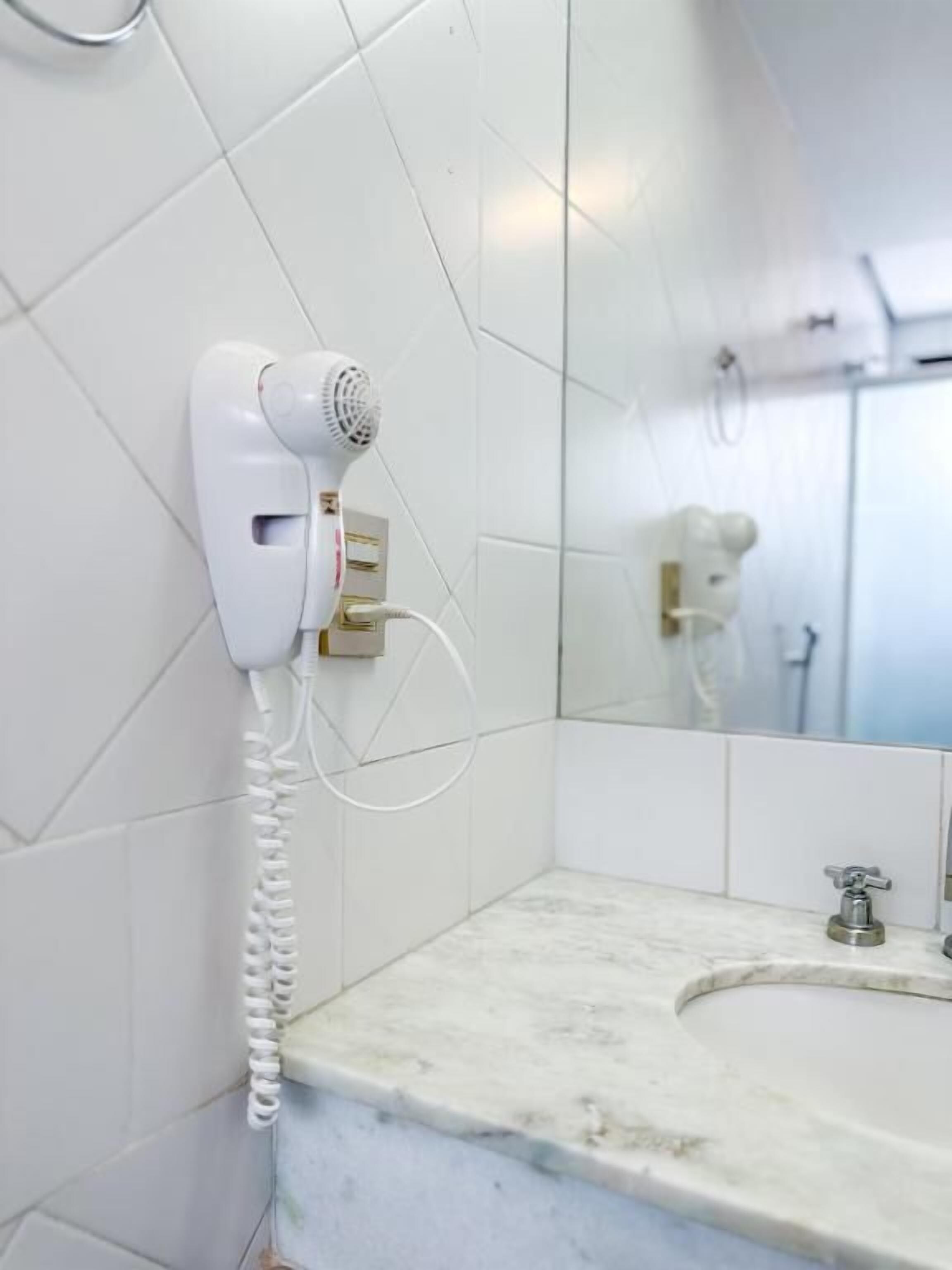 A bathroom with white tiled walls, a marble countertop, a sink, and a hairdryer mounted on the wall.
