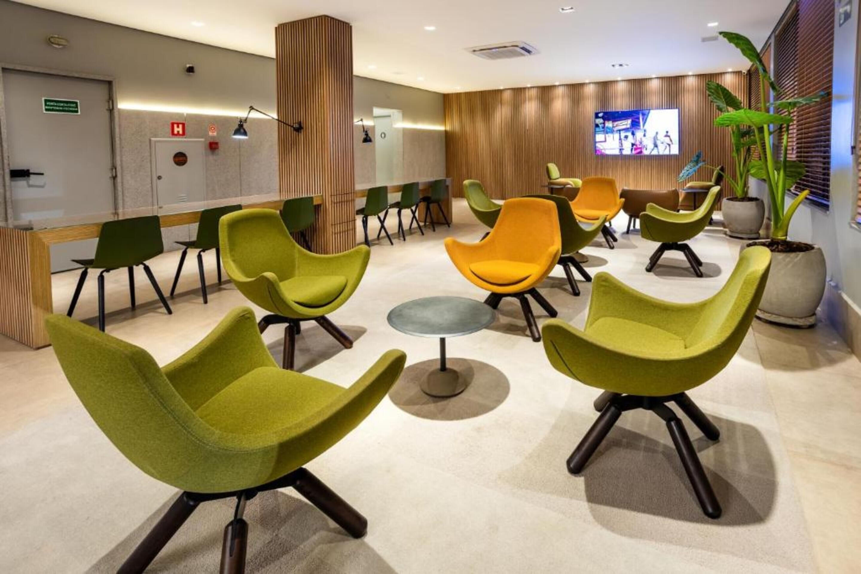 A modern waiting area with green and orange chairs, a small round table, and a television screen.
