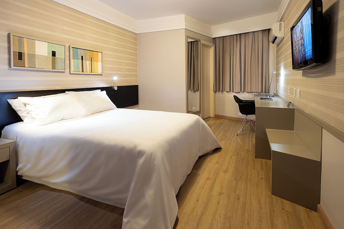 A hotel room with a bed, a desk, a chair, a television, and a mirror.