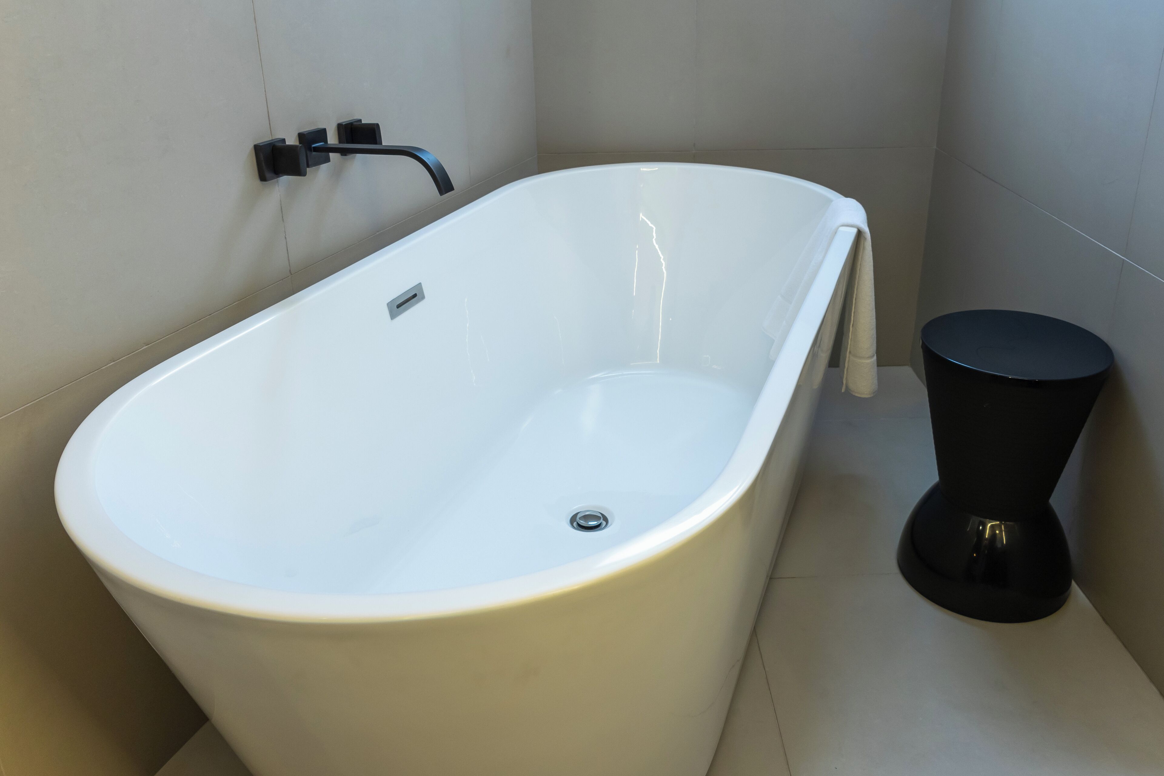 A modern bathroom with a freestanding bathtub, a black toilet, and a wall-mounted faucet.