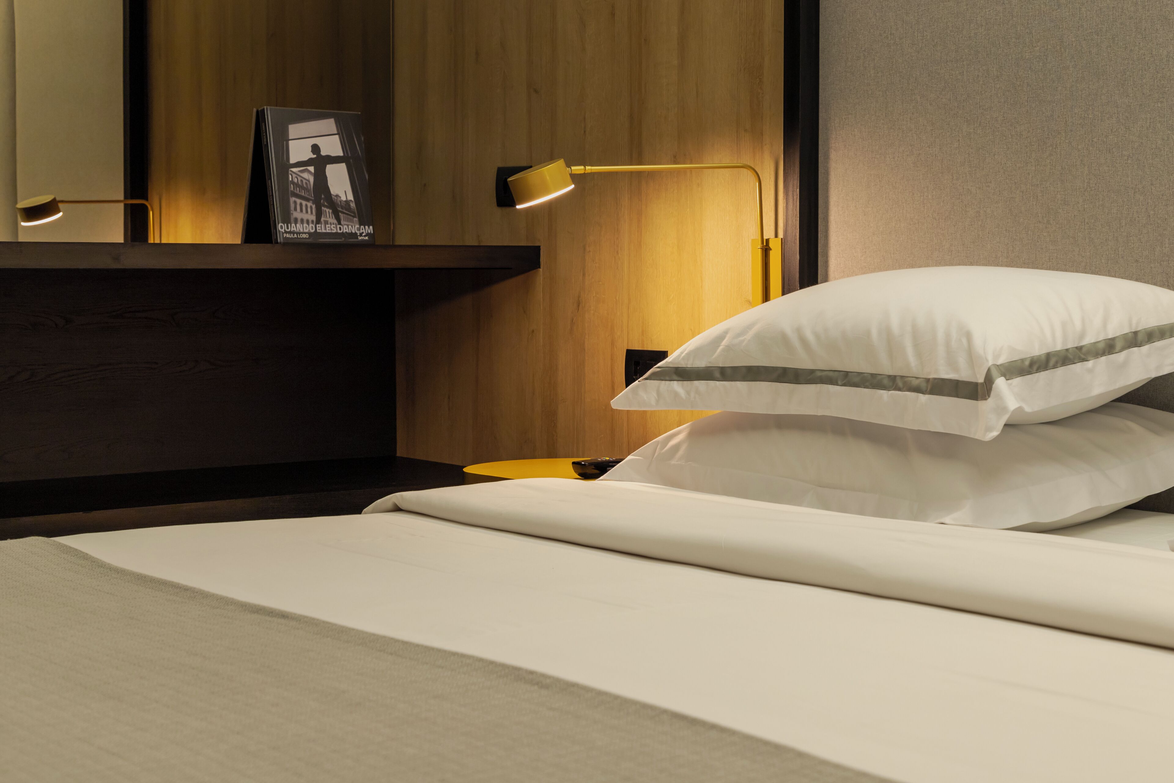 A neatly made bed with white bedding and a pillow with a gray stripe, a bedside table with a lamp, and a framed picture on the wall.