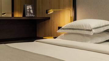 A neatly made bed with white bedding and a pillow with a gray stripe, a bedside table with a lamp, and a framed picture on the wall.