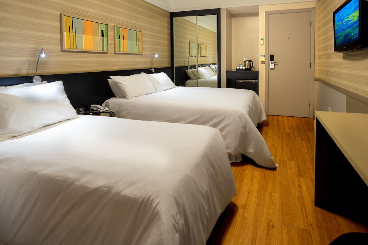A hotel room with two beds, a desk, a TV, and a mirror.