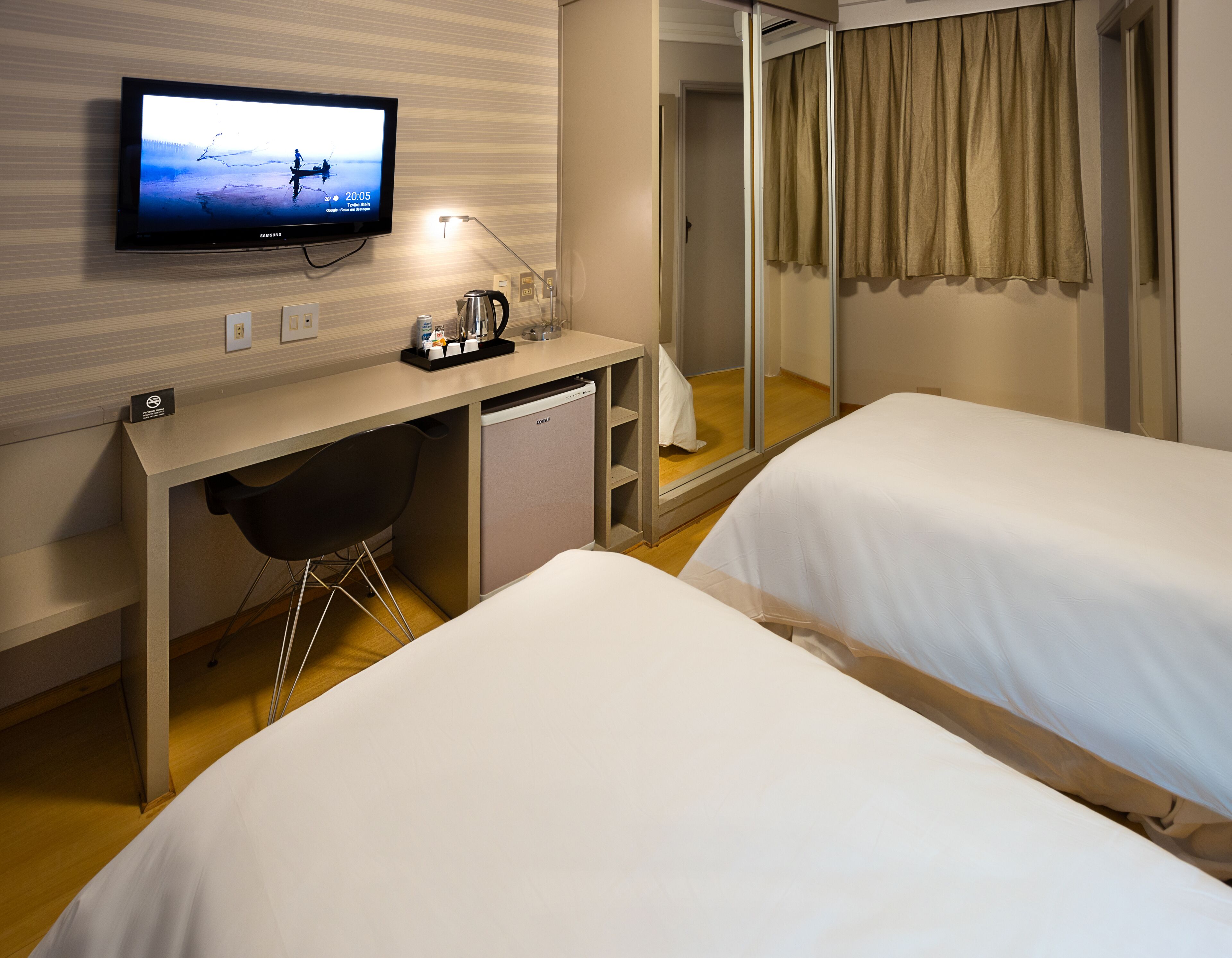 A hotel room with two beds, a desk with a computer, a television, and a minibar.