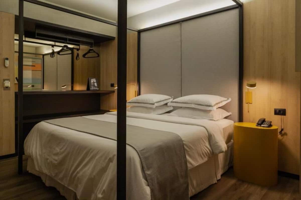 A modern hotel room with a large bed, a bedside table with a phone, and a mirror above the bed.