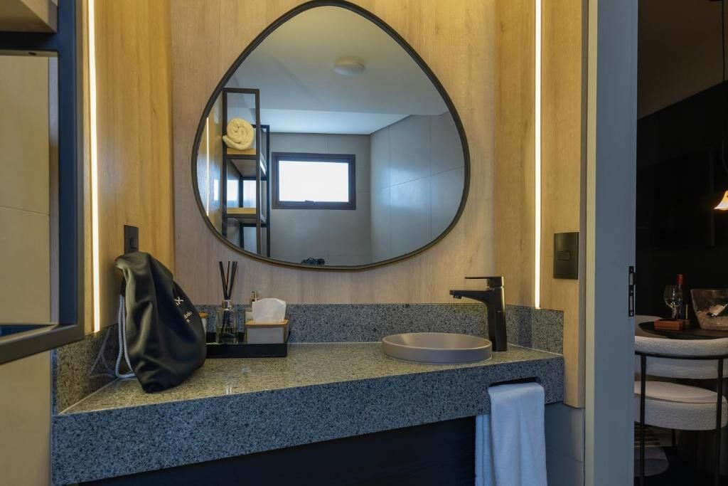 Une salle de bain moderne avec un grand miroir rond, un comptoir en granit et un petit lavabo.
