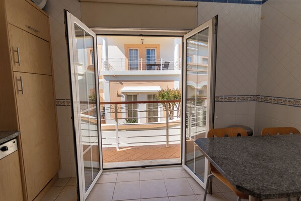 Una cocina con comedor, una puerta corrediza de vidrio a un balcón y vistas de un edificio con balcón.