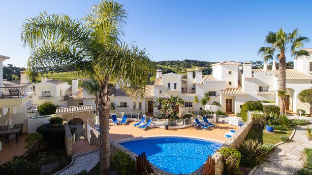 A pool area with lounge chairs, palm trees, and a clear blue sky.
