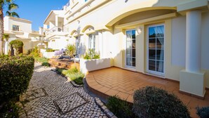 A courtyard with a paved walkway, white buildings, and greenery.