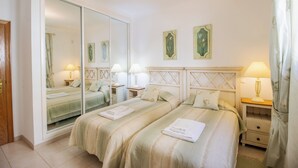 A bedroom with two beds, a large mirror, bedside lamps, and framed floral artwork on the wall.