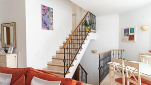 A staircase with a wooden handrail and black balusters, leading to a dining area with a white table and chairs.