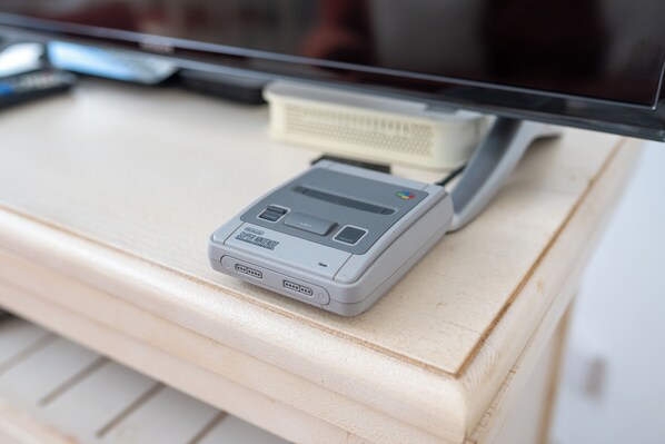 Un dispositivo portatile piccolo e grigio, con una porta USB e un display, posato su una superficie di legno vicino a un monitor.