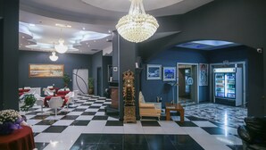 Un vestíbulo con piso a cuadros, un candelabro, un reloj, un sofá y una máquina expendedora.