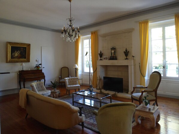 A spacious living room with a fireplace, a chandelier, and a piano.