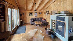 Ein gemütliches Blockhaus-Interieur mit Holzbalkendecke, Kamin, einer Couch und einem Esstisch.
