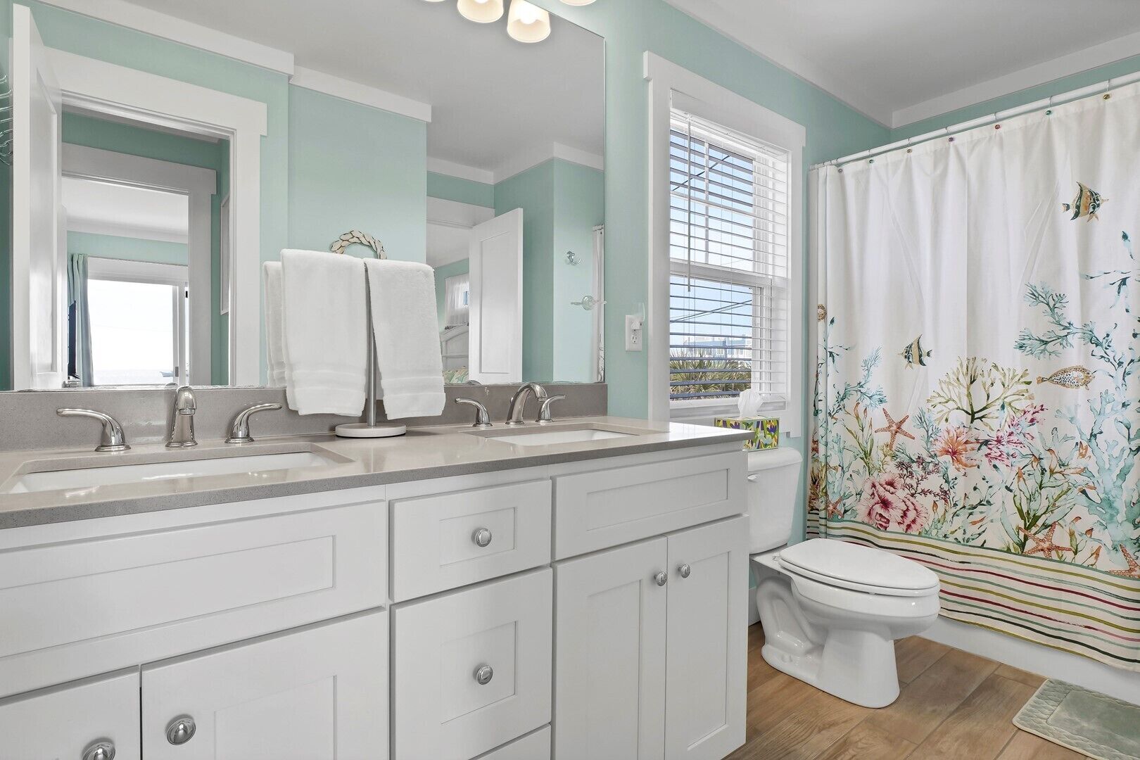 A bathroom with a double sink vanity, a toilet, and a shower curtain with a marine theme.