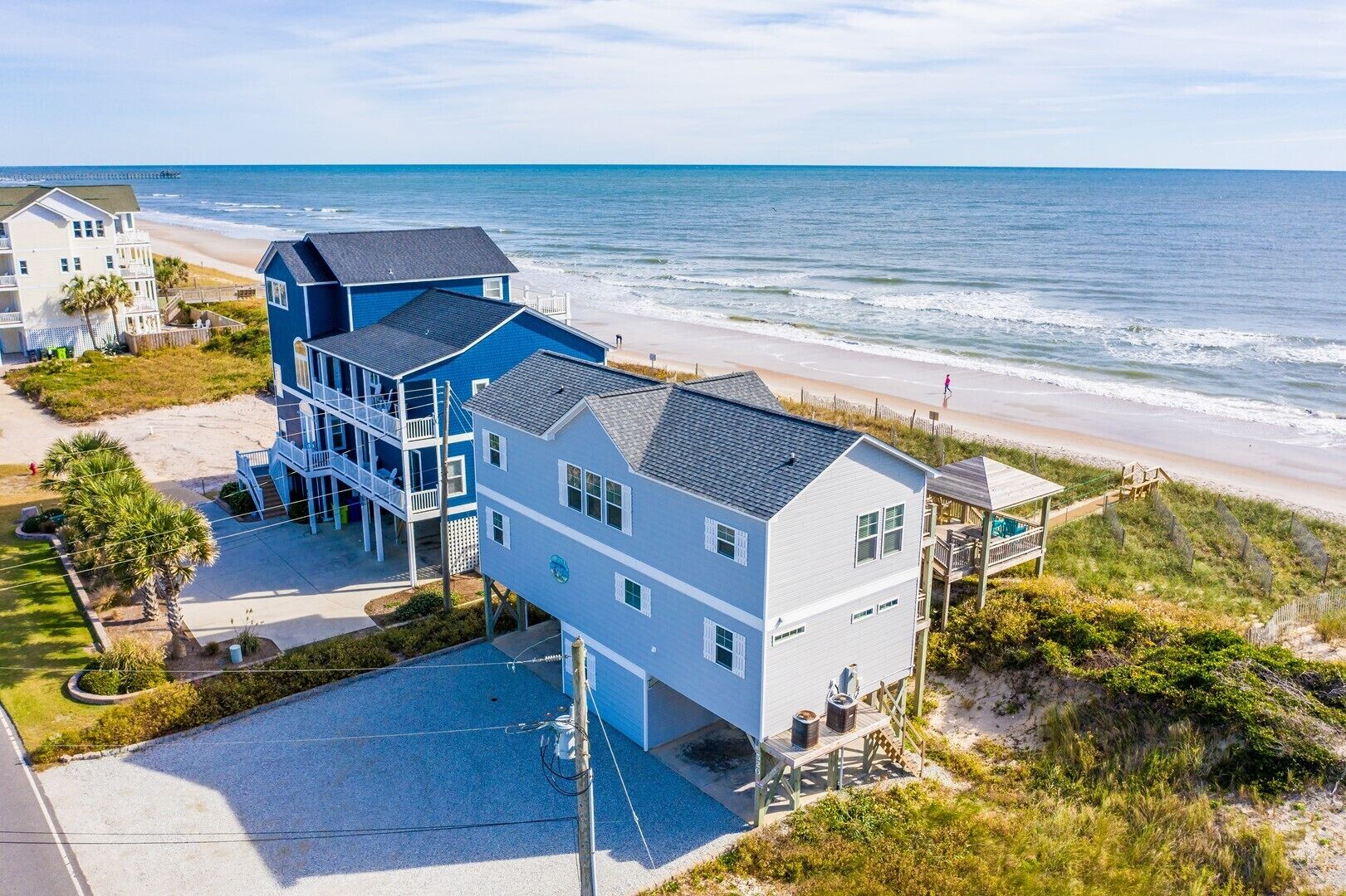 Uma casa à beira-mar com varanda de frente para a praia, entrada por um caminho de acesso e um pequeno jardim.