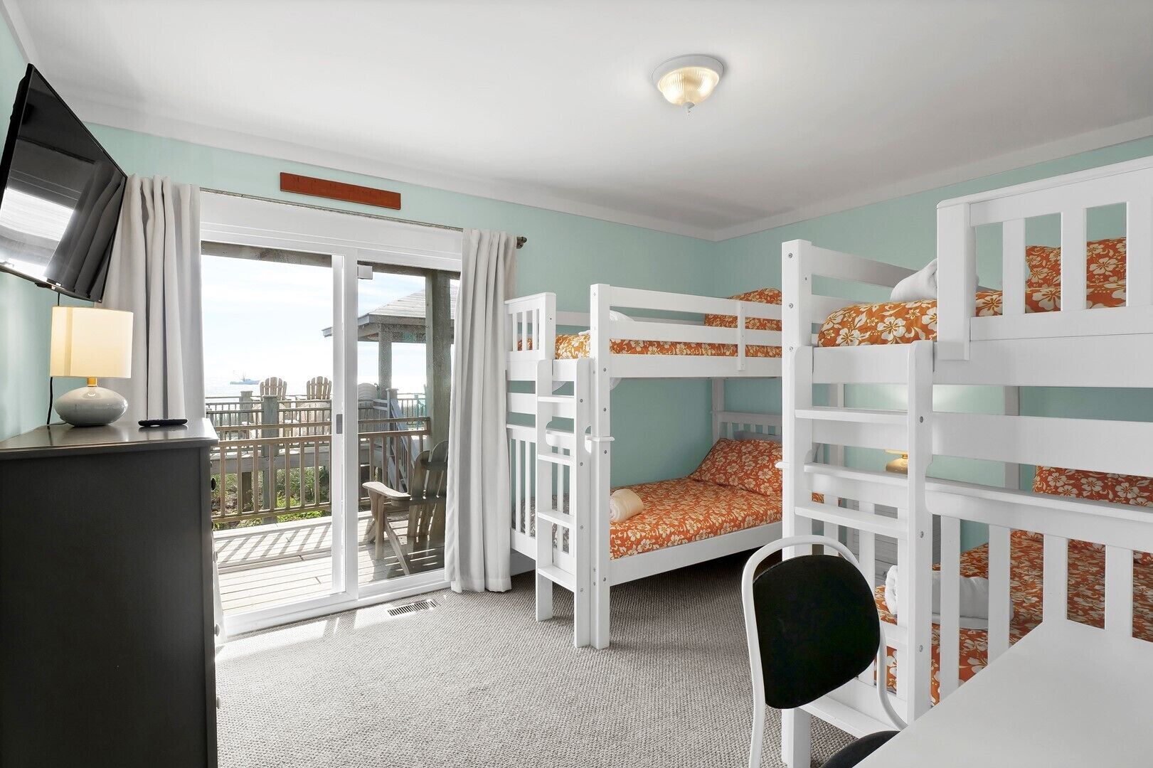 A room with bunk beds, a desk, a chair, and a view of the city.