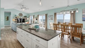 A spacious living room with a large island, a dining area with wooden chairs, and a view of the ocean. - Wright By The Sea - premier 4 bedroom oceanfront home (North Topsail Beach)