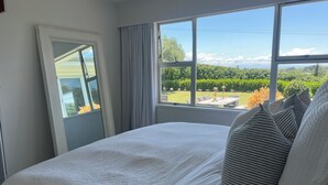 A bedroom with a large bed, a window with a view of a garden, and a door. - Private setting with vineyard outlook yet only moments from the Village.  (Havelock North)