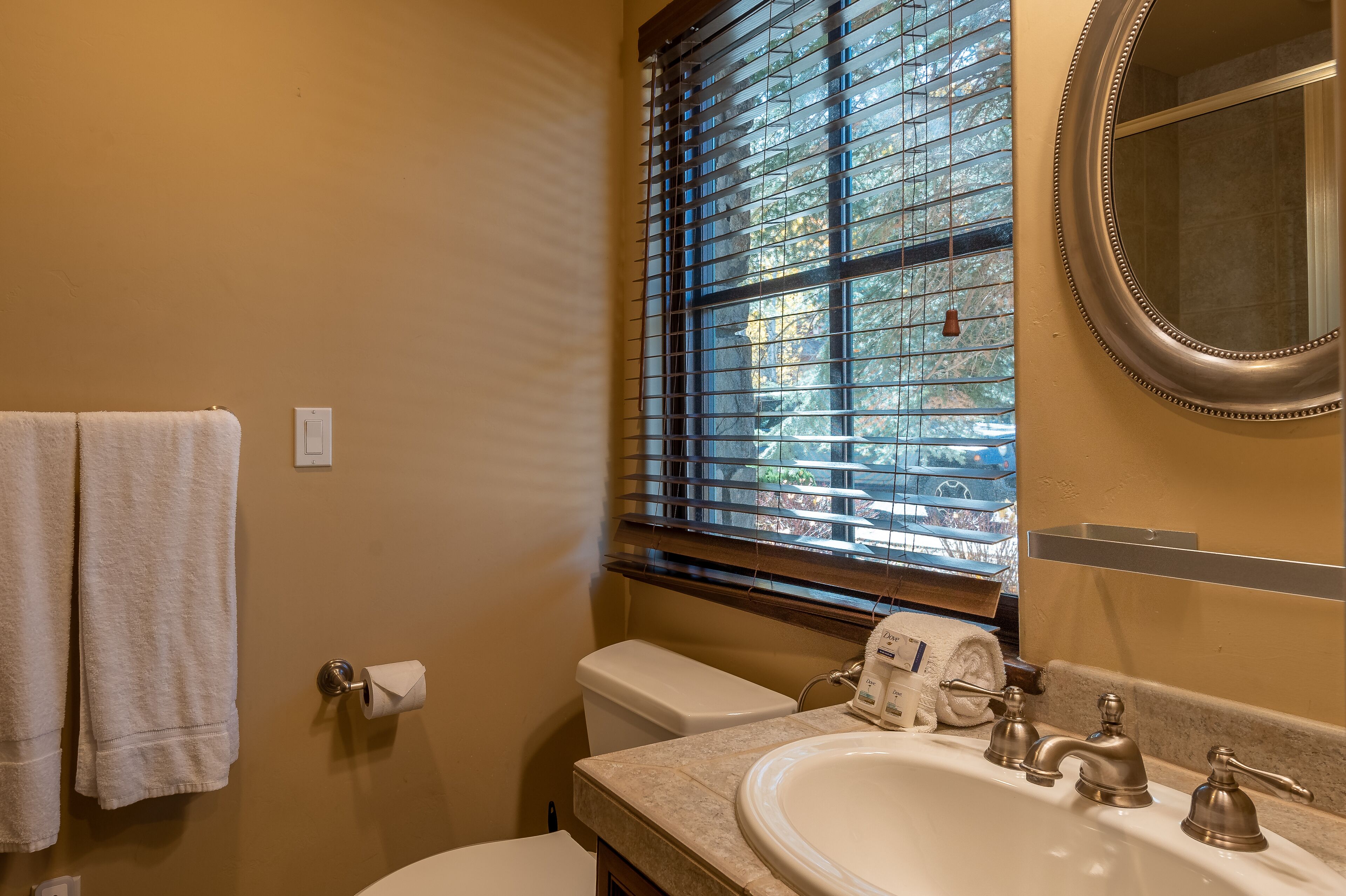 A bathroom with a toilet, sink, and window with blinds.