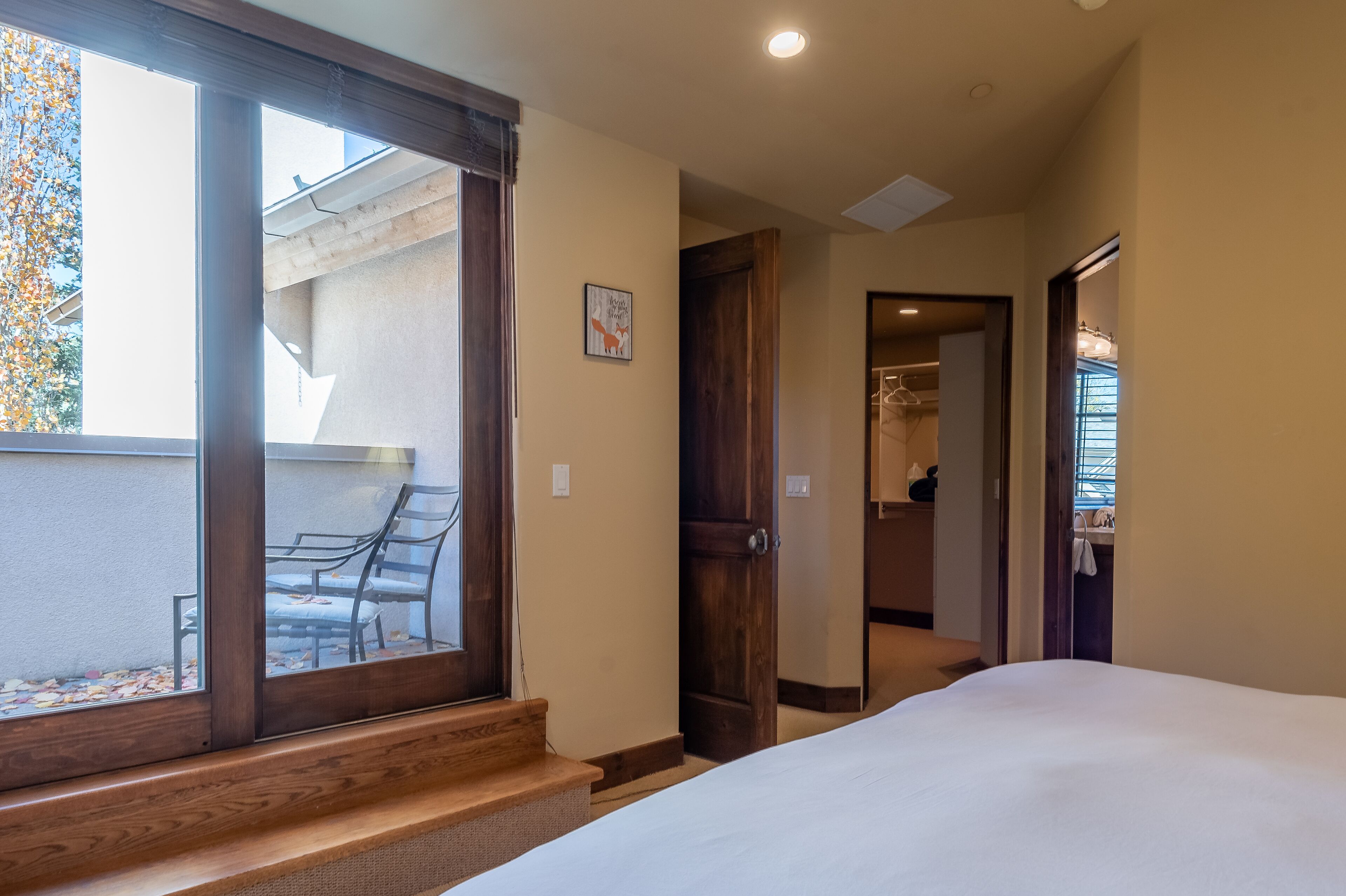 A hotel room with a large window, a bed, a wooden bench, and a door leading to a bathroom.