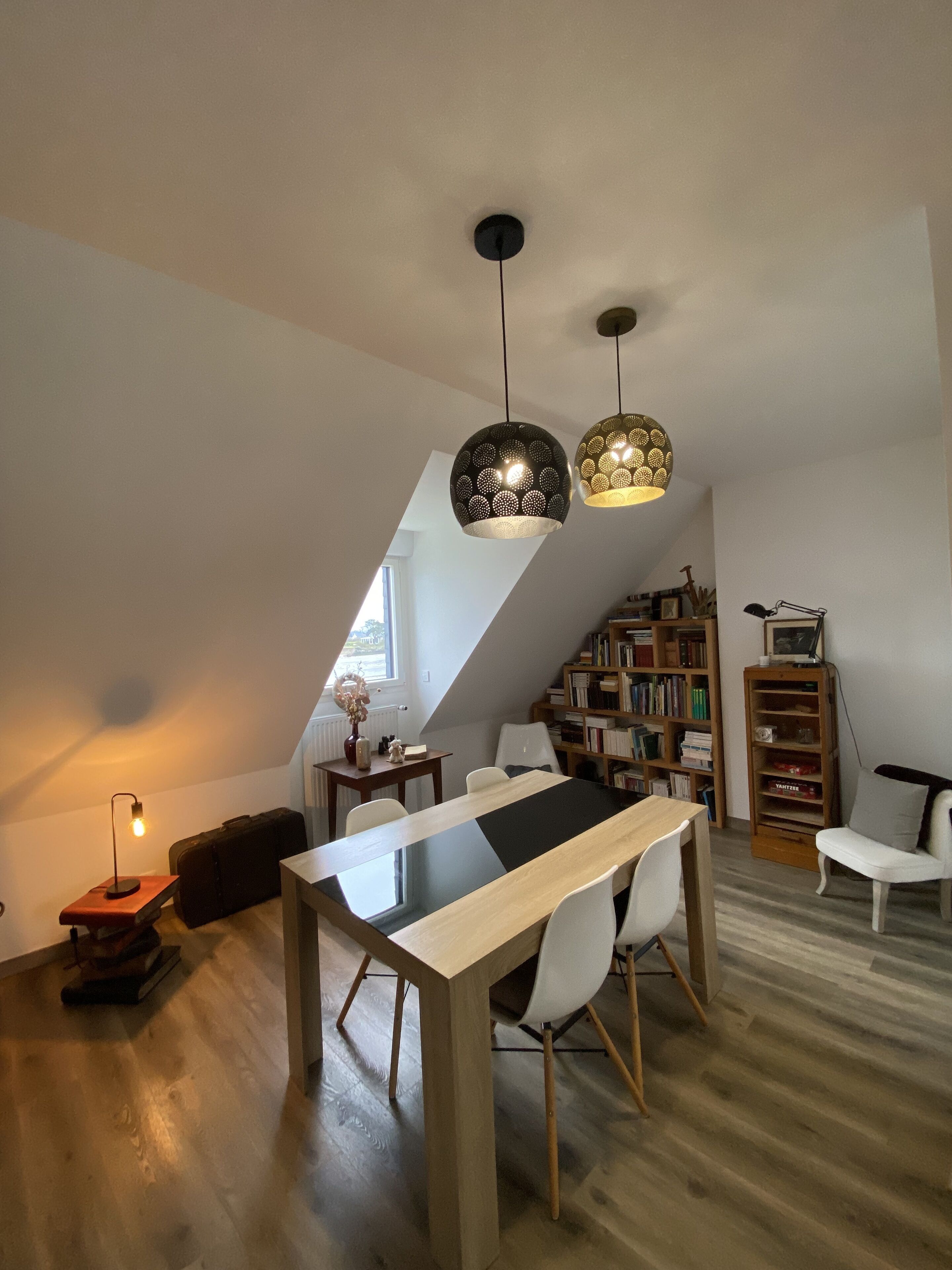 A modern loft with a dining area featuring a long table and chairs, a bookshelf, and a loft bed.