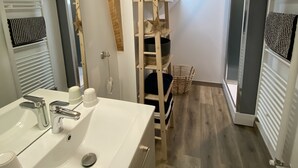 Een moderne badkamer met een grote spiegel, een witte wastafel en houten balken aan het plafond.