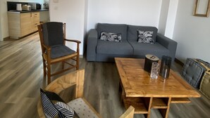 Een moderne woonkamer met een bank, twee stoelen, een salontafel en een keuken op de achtergrond.