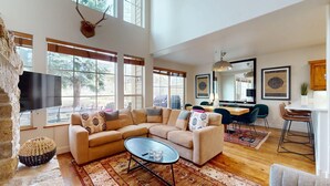 A spacious living room with a large sectional sofa, a flat-screen TV, and a stone wall. - Central Park 26- Luxury Tri-Level in Great Location Close to River Run (Ketchum)