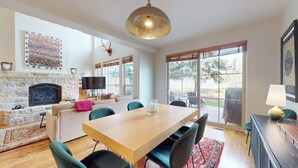 A spacious living area with a stone fireplace, a wooden dining table, and a large window offering a view of the outdoors. - Central Park 26- Luxury Tri-Level in Great Location Close to River Run (Ketchum)