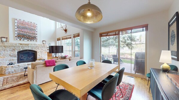 Un vaste espace de vie agrémenté d’une cheminée en pierre, d’une table à manger en bois et d’une grande fenêtre offrant une vue sur l’extérieur.