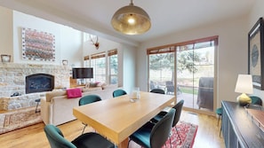 Un salón amplio con chimenea de piedra, una mesa de comedor de madera y un ventanal con vistas al exterior.
