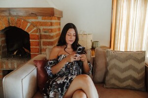 A person sitting on a sofa in a room with a brick fireplace and a window with curtains.