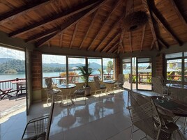 Amplio espacio interior con techo alto y ventanas grandes que ofrecen vistas a un lago y montañas.