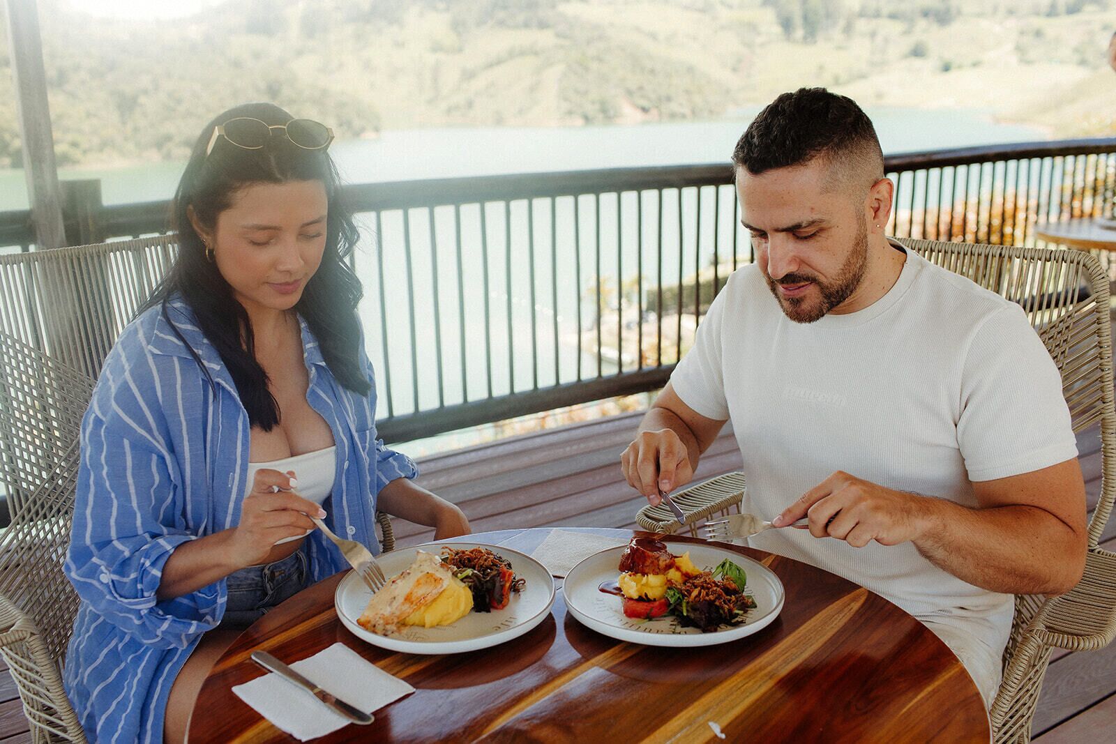 Two people dining at an outdoor table with a view of a natural landscape.