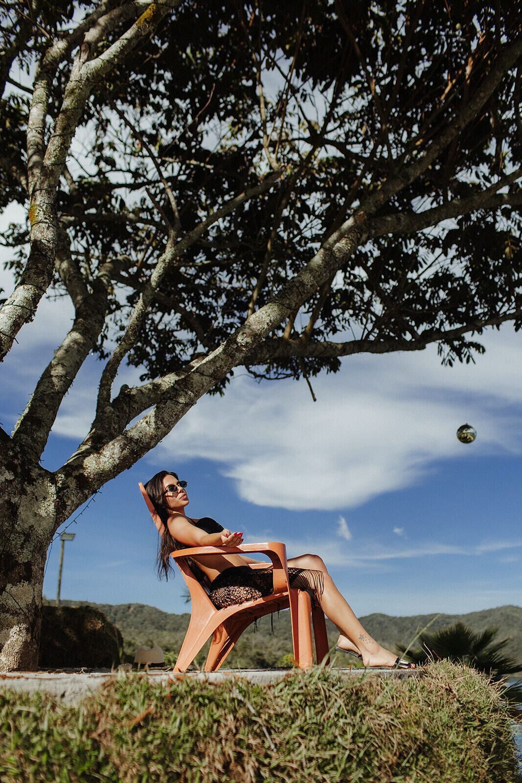 Una persona sentada en una silla bajo un árbol, con un cielo despejado al fondo.