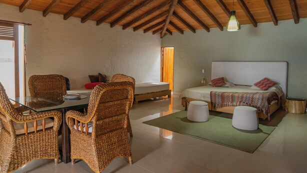 A room with a wooden ceiling, a bed with pillows, a table with chairs, and a small round table. - Kuma Secret Island - Experience Hotel (Guatapé)