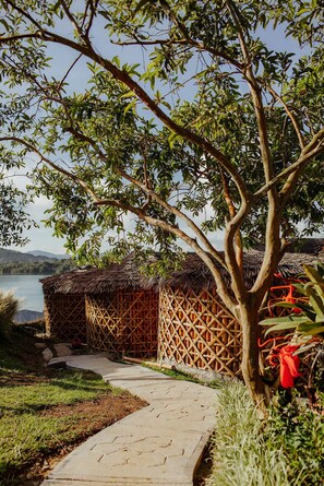 A pathway leading to a thatched-roof structure surrounded by lush greenery and a tree. - Kuma Secret Island - Experience Hotel (Guatapé)