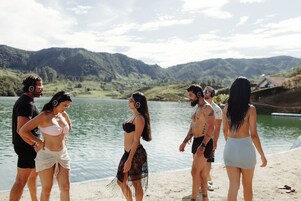Un grupo de personas de pie junto a un lago con montañas al fondo.