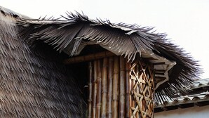 A traditional thatched-roof hut with a bamboo lattice structure, a door, and a small garden area with grass and plants. - Kuma Secret Island - Experience Hotel (Guatapé)
