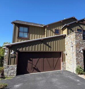Une maison à deux étages avec un garage, des éléments décoratifs en pierre et un ciel dégagé.