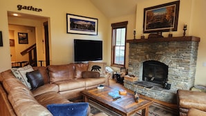 A cozy living room with a stone fireplace, leather sofa, and a flat-screen TV.