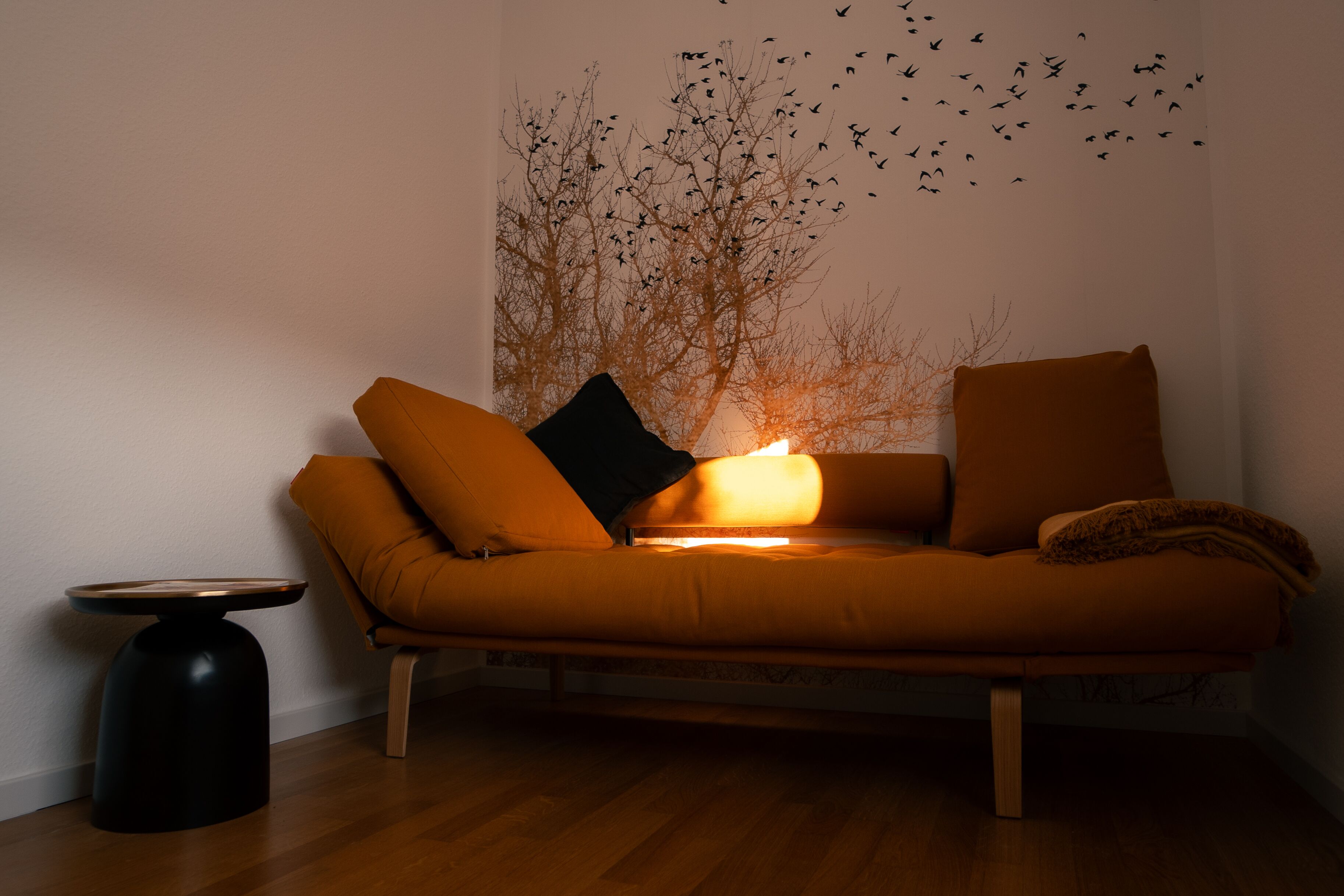 A cozy living room with a sofa, a side table, and a wall mural.
