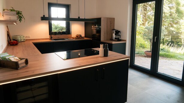A modern kitchen with a central island, built-in appliances, and a large sliding glass door to a garden.